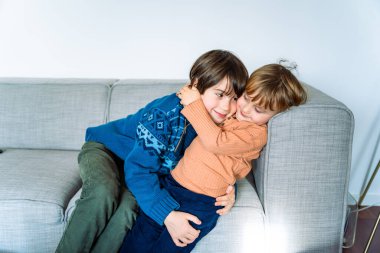 İki kardeş evdeki kanepede uzanıyor, gülümsüyor ve sarılıyorlar. Kardeşler arası iyi ilişkiler. Çocukları kucaklamak.