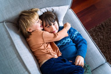 İki kardeş evdeki kanepede uzanıyor, gülümsüyor ve sarılıyorlar. Kardeşler arası iyi ilişkiler. Çocukları kucaklamak.