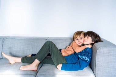 İki kardeş evdeki kanepede uzanıyor, gülümsüyor ve sarılıyorlar. Kardeşler arası iyi ilişkiler. Çocukları kucaklamak.