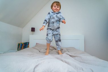 Evdeki yatak odasında oynayan üç yaşında sevimli bir çocuk. Mutlu çocuk yatağa atlıyor ve jimnastik yapıyor. Çocuklarla evde vakit geçirmek.