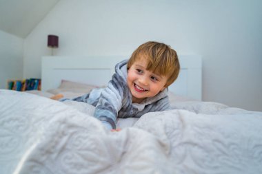 Küçük sarışın çocuk, yatakta dinleniyor. Ev tatili. Gülen çocuk yatakta oynuyor..