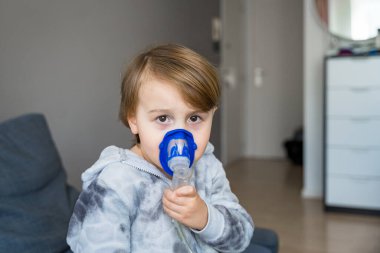 Hasta çocuk evde solunum yapıyor, yürümeye yeni başlayan çocuk nebulizör kullanarak terapi spreyi kullanıyor. Soğuk algınlığı ve zatürree tedavisi kavramı.