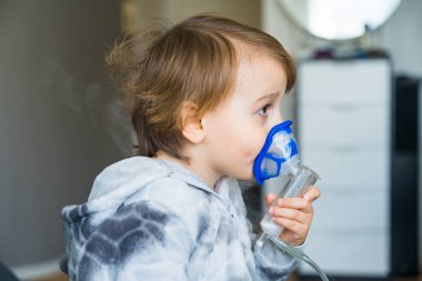 Hasta çocuk evde solunum yapıyor, yürümeye yeni başlayan çocuk nebulizör kullanarak terapi spreyi kullanıyor. Soğuk algınlığı ve zatürree tedavisi kavramı.