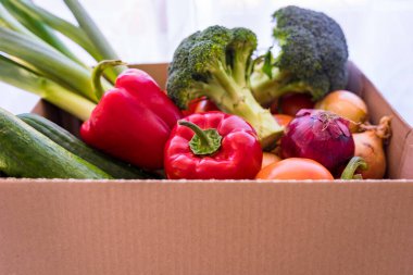 Karton bir kutuda farklı taze sebzeler. Coronavirus karantinası sırasında yiyecek teslimatı. Brokoli, pırasa, salatalık, dolmalık biber, domates, soğan süpermarketten alınmış..