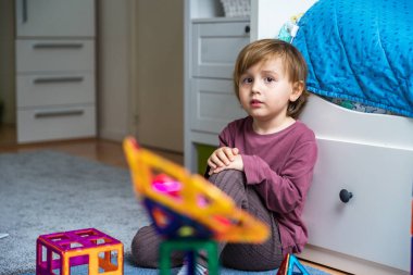 Küçük üzgün çocuk karantina sırasında odada tek başına oturuyor. Çocuk sıkılmış ve melankolik. Bebek evde yerde oturuyor, kameraya bakıyor..