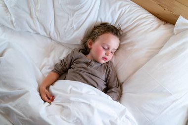 Pijama giyen küçük anaokulu çocuğu evdeki yatakta uyuyor. Çocuk sabahları uyanmak istemiyor..