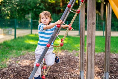 Parkta oynayan tatlı küçük bir çocuk. Yeni yürümeye başlayan çocuk kaydırağa tırmanırken yüzünü kaçırıyor. Çocuklar için yaz etkinlikleri.