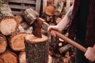 Kareli gömlekli dövmeli adam paslı balta tutuyor.