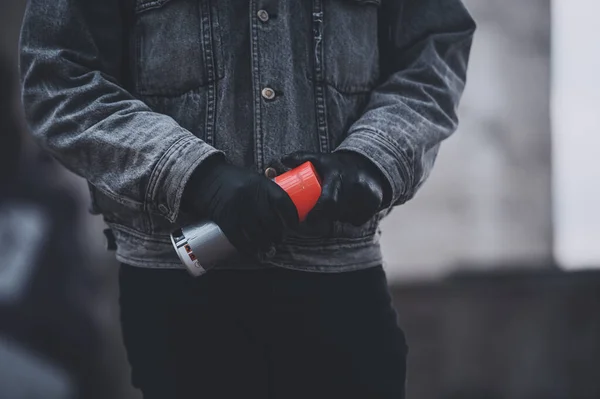 Man in gloves and denim jacket takes a spray paint. Gray days of graffiti artist — Stock Photo, Image