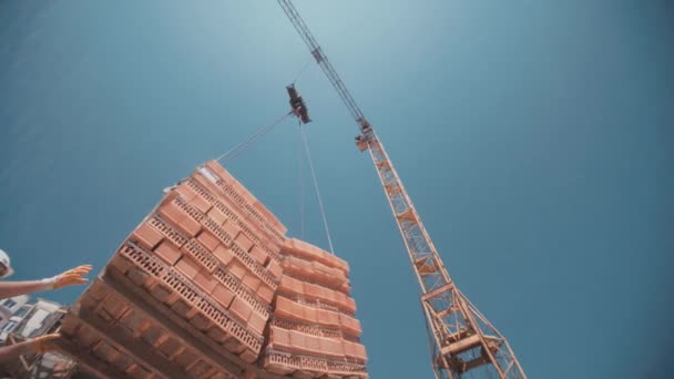Los trabajadores clavaron bloques de ladrillos rojos levantados por una grúa — Vídeo de stock