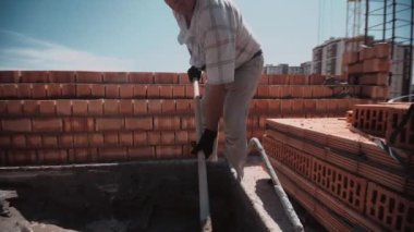 Yaşlı adam kürekle çimentoyu alır ve onu yapmak için kırmızı tuğla duvara yerleştirir. 