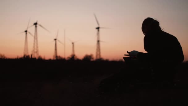 Chica con silueta portátil en el fondo de molinos de viento y hermosa puesta de sol — Vídeo de stock