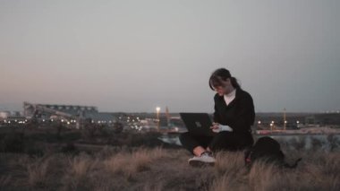 Endüstriyel bölgedeki tepelerde defterle yazan kıza bak.