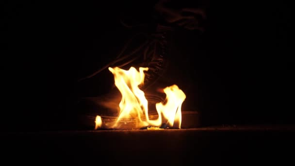Az ember a nehéz csizmájával oltja el a tüzet a földön. Sötét jelenet — Stock videók