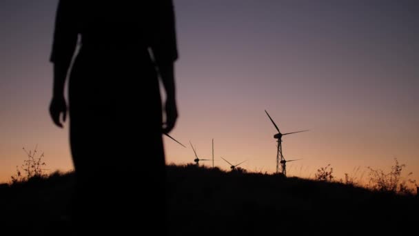 Camminando ragazza sulle colline del tramonto vicino ai generatori di energia eolica — Video Stock