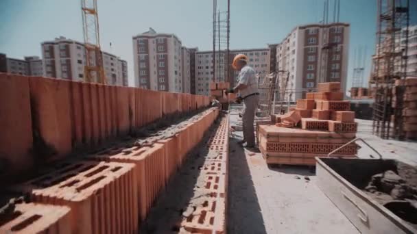 Umzug entlang einer Mauer aus roten Ziegeln zu einem Bauunternehmer, der sie baut — Stockvideo