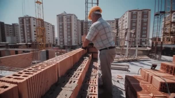 Oudere bouwer man gebruikt cement om beton een rode bakstenen muur — Stockvideo