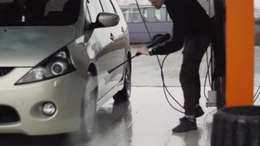 Genç adam arabasının tekerleklerini temizlemek için yüksek basınçlı su jeti kullanıyor.
