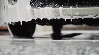 Araba yıkama yerinde bir arabadan beyaz köpük damlaları düşüyor.