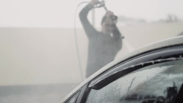 Genç ve şık bir adam arabasını temizlerken araba yüzeyinde bir sürü sıçrama oluyor. — Stok video