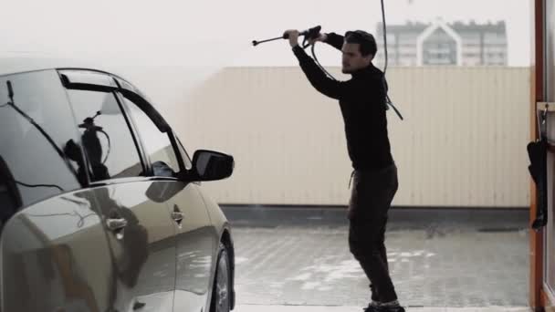 Junge stilvolle lockige Kerl verwendet einen Hochdruckstrahl Wasser, um ein Auto zu reinigen — Stockvideo