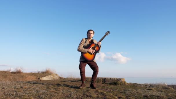 Смайлі хлопець стрибає з гітарою на узбережжі в сонячний весняний день — стокове відео