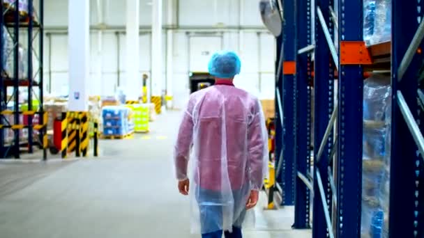 Un datore di lavoro in tuta bio protettiva cammina vicino a scaffali blu su un grande magazzino — Video Stock