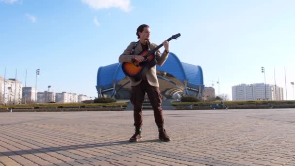 Energetikus stílusos fiatalember álmodozó gitározik a téren — Stock videók