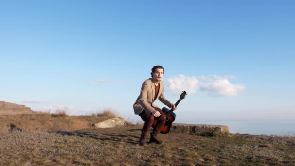 Заохочений молодий чоловік тримає стару гітару, божевільний стрибок на пагорбах у повільному русі — стокове відео