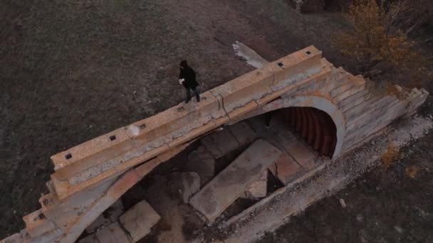 Человек в капюшоне остается на крыше разрушенного ангара на военном аэродроме — стоковое видео