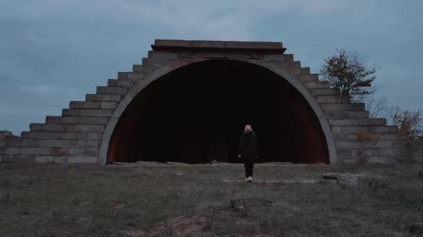 Chica rubia solitaria camina a un hangar destruido perdido en otoño. — Vídeo de stock