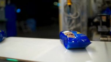  Blue packs of pasta fall on a conveyor line after packing machine