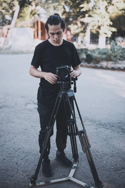 Stylish young operator in black works outdoor with a camera — Stock Photo, Image