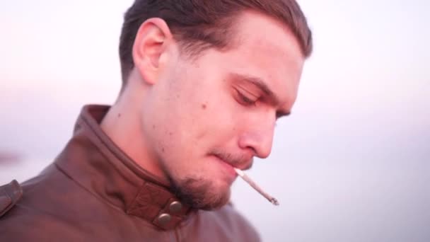 Порядочный молодой человек в защитном костюме байкера нервничает, пытаясь зажечь сигарету. — стоковое видео