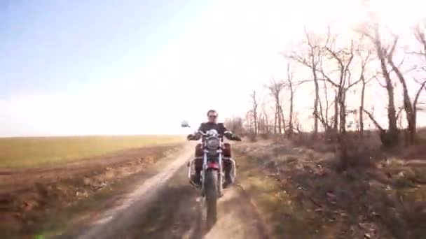 英俊的男子在穿过田野的土路上骑着一辆红色咖啡店的摩托车 — 图库视频影像
