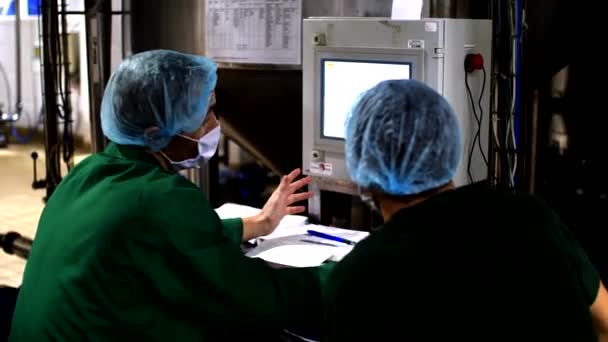 Zwei Fabrikarbeiter in Schutzanzügen sitzen in der Nähe eines Kontrollbildschirms — Stockvideo