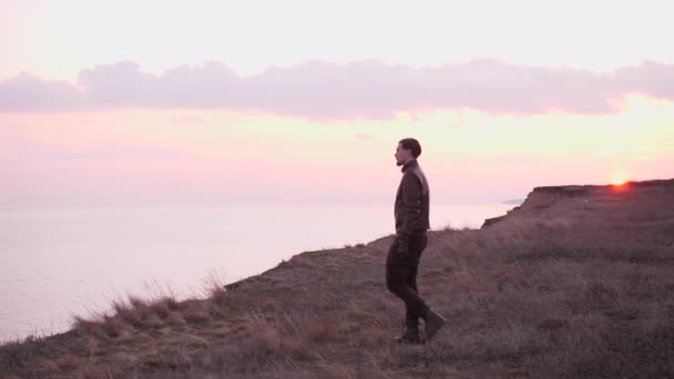 Tittar på ung cyklist i läderkostym går till ett stup över havet i solnedgången — Stockvideo