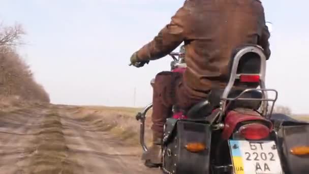 Szybka jazda polną drogą, za motocyklistą na czerwonym śmigłowcu, przez jesienne pola — Wideo stockowe