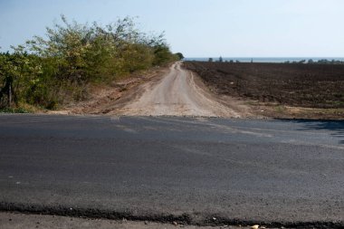 View of the half-asphalt crossroad on the field near the sea