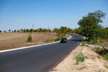 Black car moves on the new road at the sunny valley