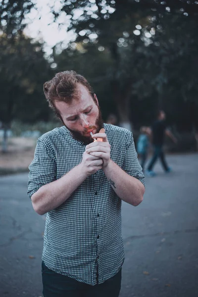 Bearded man in checker shirt lights up weed in public place 