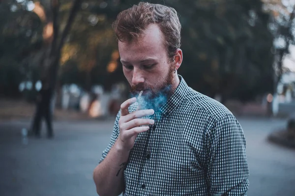 Stylish young bearded man smokes joint in the park. — Stock Fotó