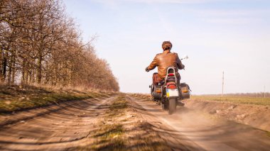 Deri ceketli bir adam sonbahar güneşli bir günde helikopterle off-road 'a biniyor.