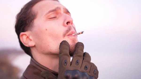 Érzelmi portré egy göndör jóképű férfiról élvezze a kézzel sodort marihuána ízületet. Stock Kép