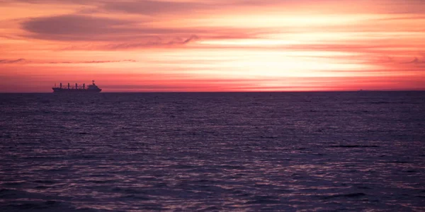 Prise de vue du coucher de soleil orange-rouge parfait au-delà des nuages près des vagues sombres de la mer. Photos De Stock Libres De Droits