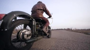 Deri ceketli havalı bir adamın klasik motosiklet sürüşünün yan görüntüsü.