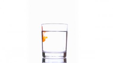 Ağaç damlaları saf su bardağına damlayan turuncu kırmızı mürekkep damlaları.