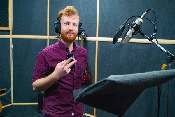 Jeune homme barbu rester près du microphone, enregistrement de la voix dans un studio professionnel Image En Vente