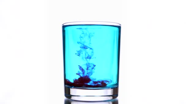 Gotas de tinta roja caen en un vaso con agua azul claro. — Vídeos de Stock