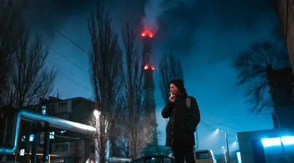 Shoot of a smoking modern man in hooded coat with industrial zone on background Zdjęcia Stockowe bez tantiem